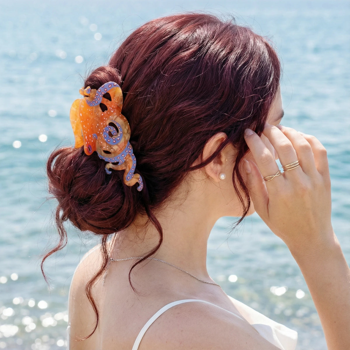 Une femme aux cheveux roux, vue de dos, tient sa main près de son visage, portant des pinces à cheveux en forme d'octopus col