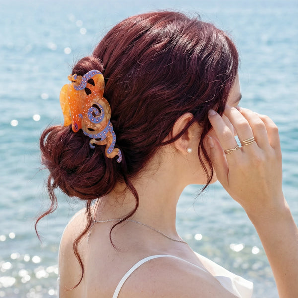 A woman with reddish hair is shown from the back, holding her hand near her face, wearing colorful octopus hair claw clips.