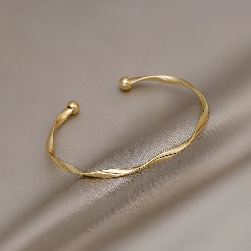 A minimalist gold-tone twisted cuff bangle displayed against a neutral background.