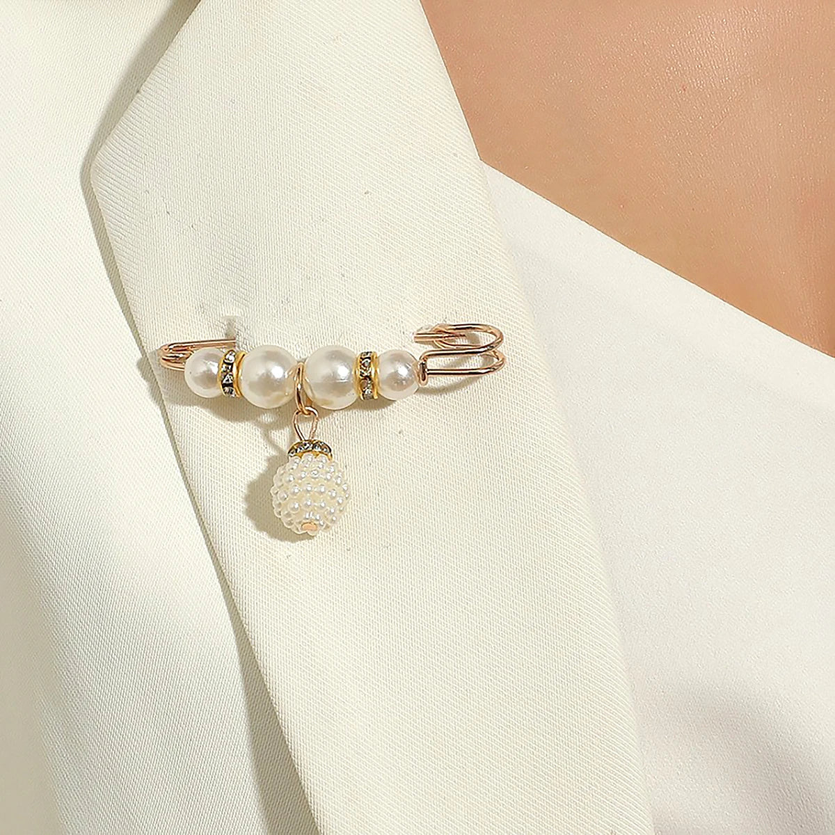 A delicate gold-toned adjustable pearl brooch featuring a cluster of round pearls and a dangling pearl, worn on a white dress