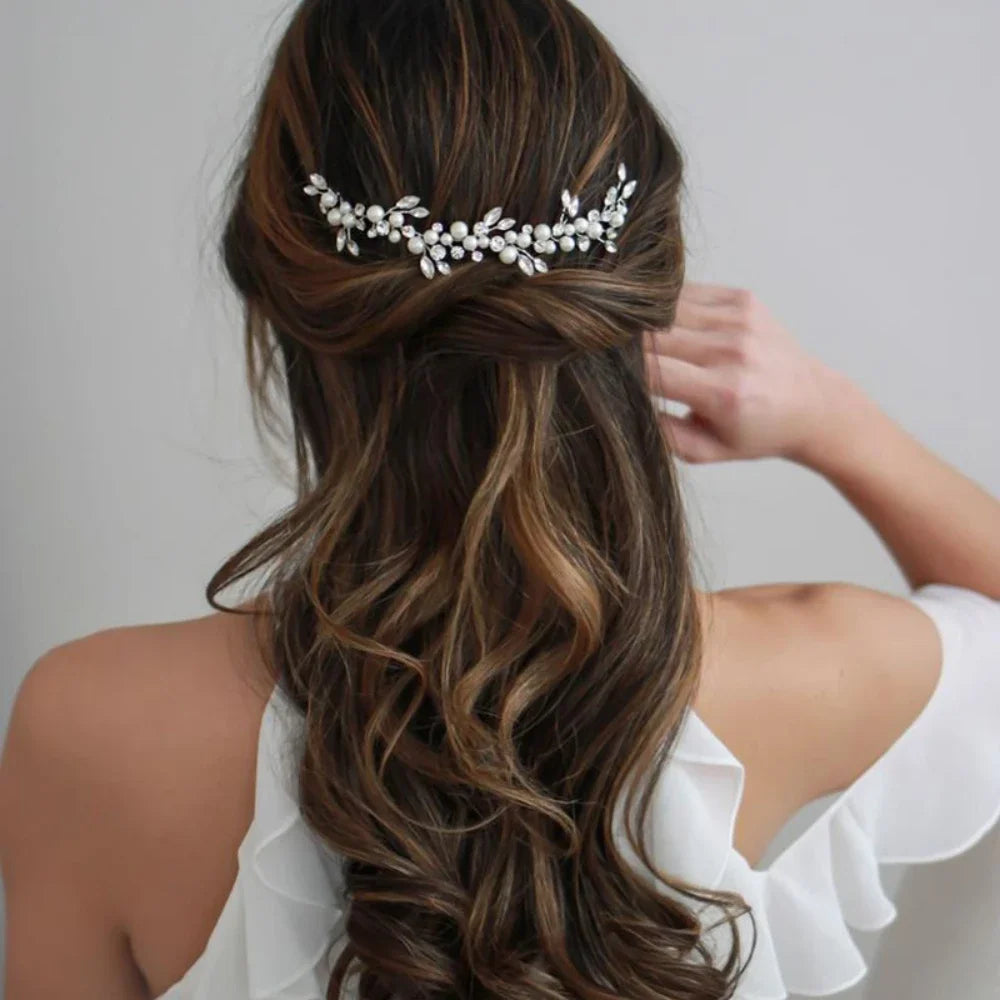 A woman's long brown hair is styled in an elegant low braid with a delicate pearl bridal headband.