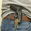 A tactical pistol keychain with a detachable holster is clipped to a brown leather belt and worn over a gray shirt.