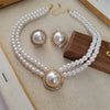 Un collier de perles élégant et des boucles d'oreilles à clous assorties avec des accents de strass, présentés sur une surfac