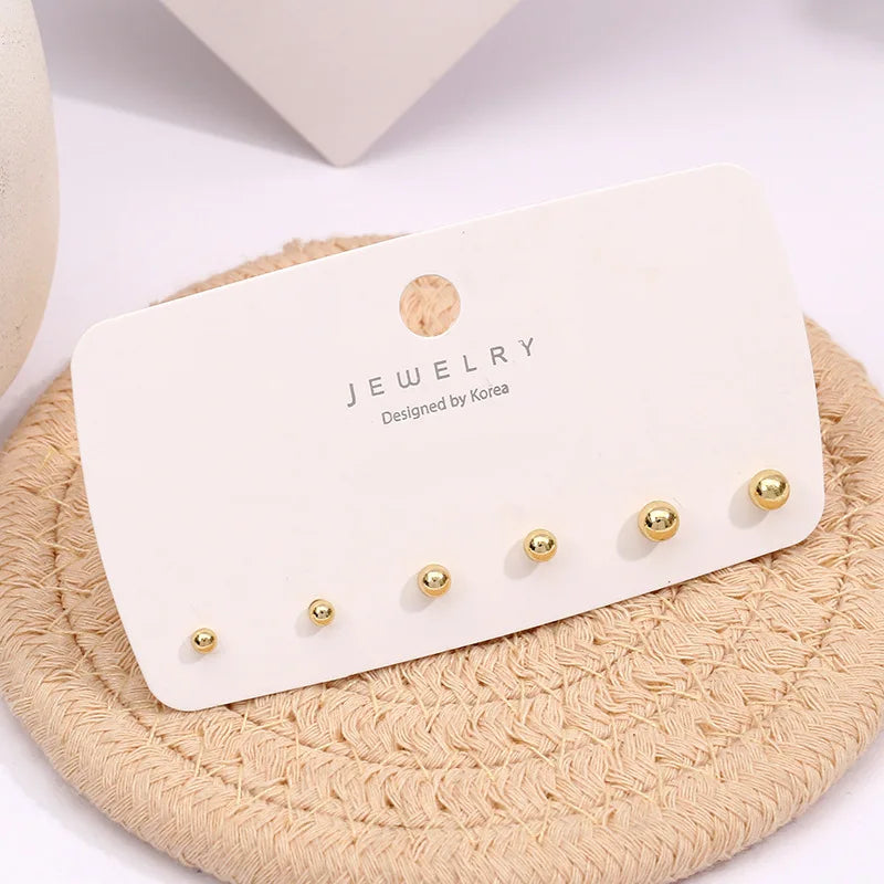 A display of three gold-toned round stud earrings on a white card resting on a beige woven surface.