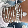 A stack of silver round beaded bracelets worn on a wrist, with a silver heart charm visible.