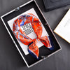 An orange and blue floral print silk scarf tied in a bow displayed in a black jewelry box.