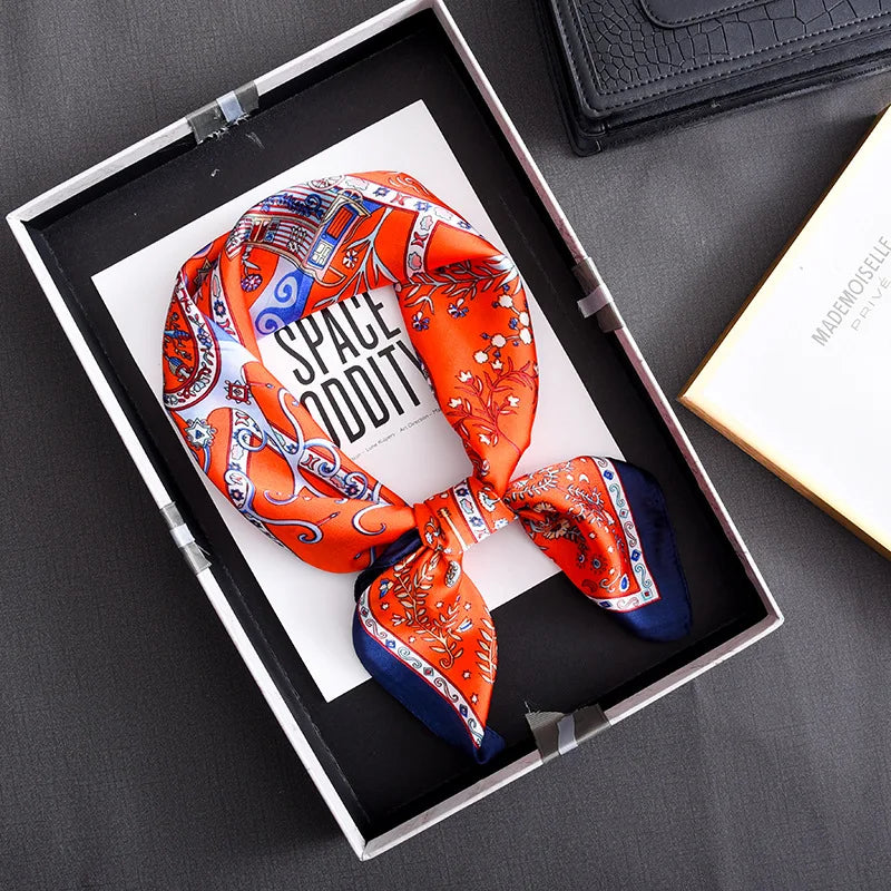 An orange and blue floral print silk scarf tied in a bow displayed in a black jewelry box.