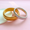 Two stacked gold and silver stainless steel elastic bangle bracelets resting on a pink surface.