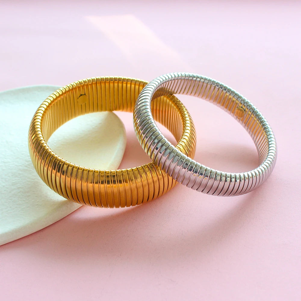 Two stacked gold and silver stainless steel elastic bangle bracelets resting on a pink surface.