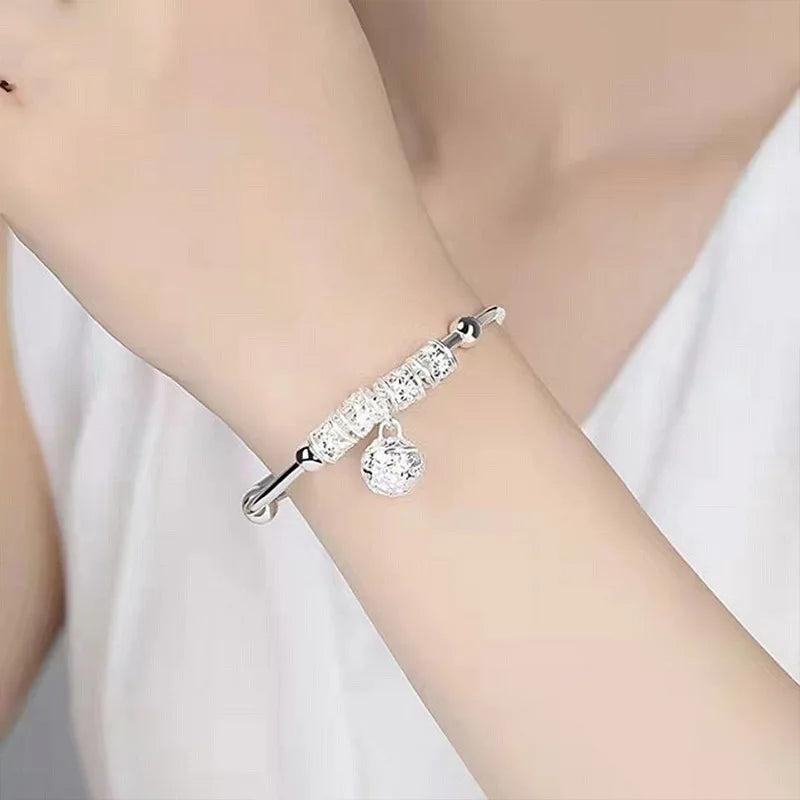 A close-up of a woman's wrist wearing delicate sterling silver bell bangles with clear stones.