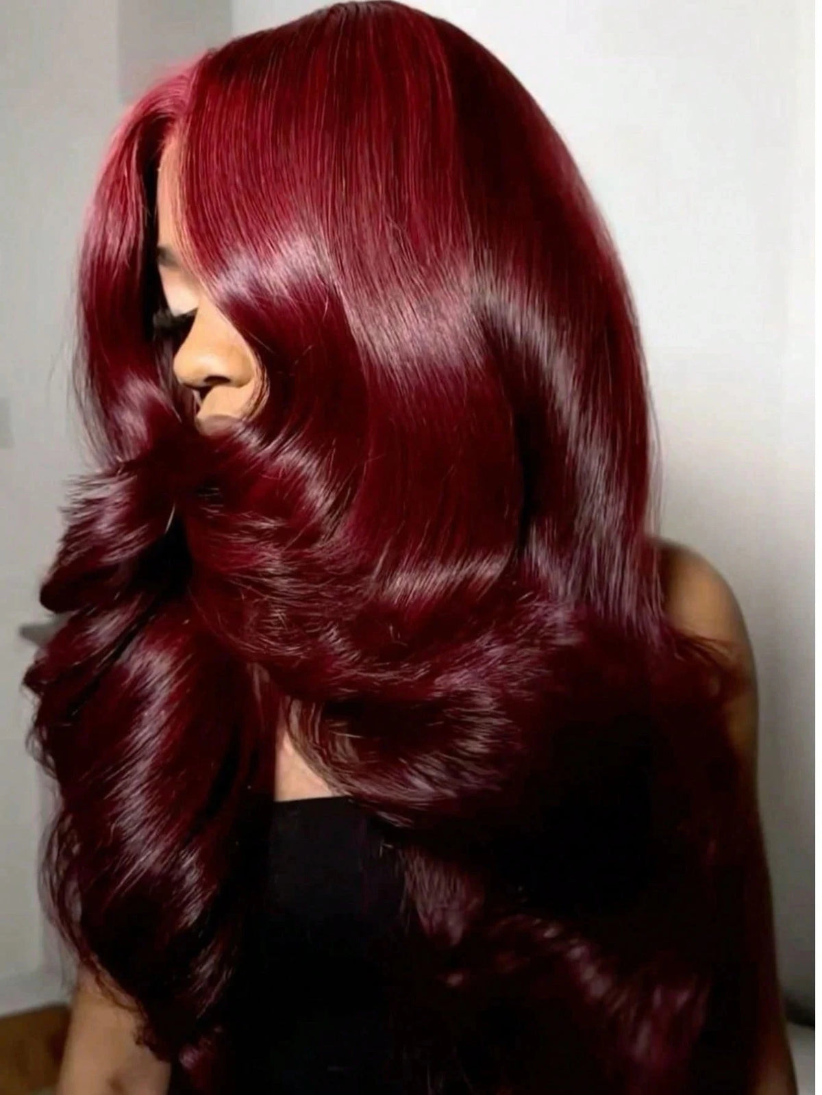A close-up of a woman with long, wavy burgundy hair looking over her shoulder.