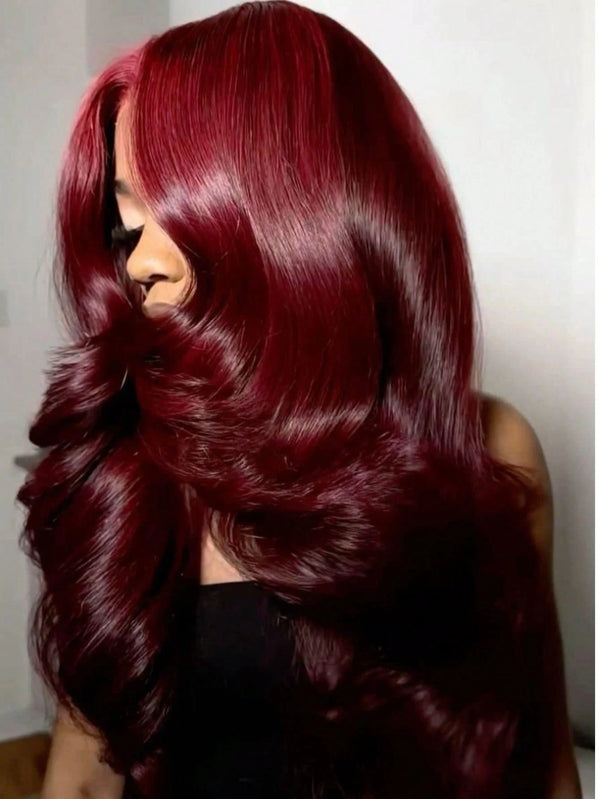 A close-up of a woman with long, wavy burgundy hair looking over her shoulder.