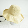 A light yellow hand-woven straw visor hat is displayed on a white surface.