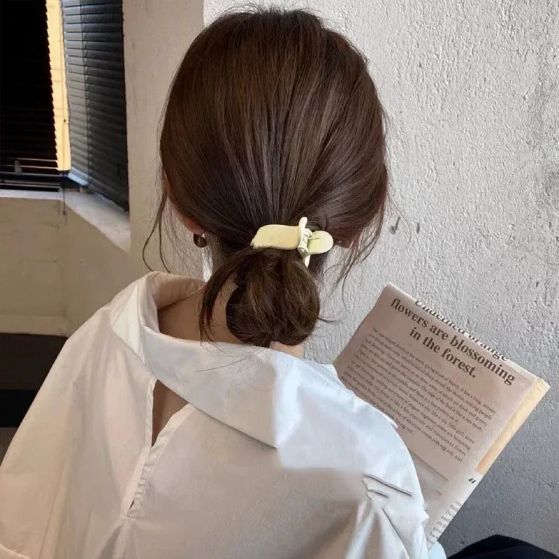 A woman with brown hair tied in a ponytail is shown from the back, wearing a white shirt and holding a book.