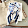 A blue and white striped silk scarf tied in a bow displayed on a white card next to a beige blazer.