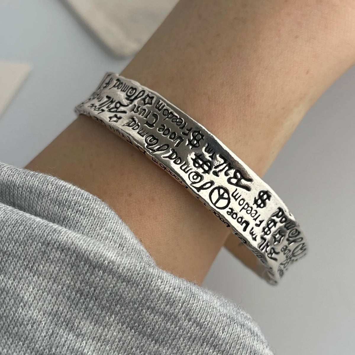 A close-up of a sterling silver charm bracelet worn on a wrist, featuring engraved text.