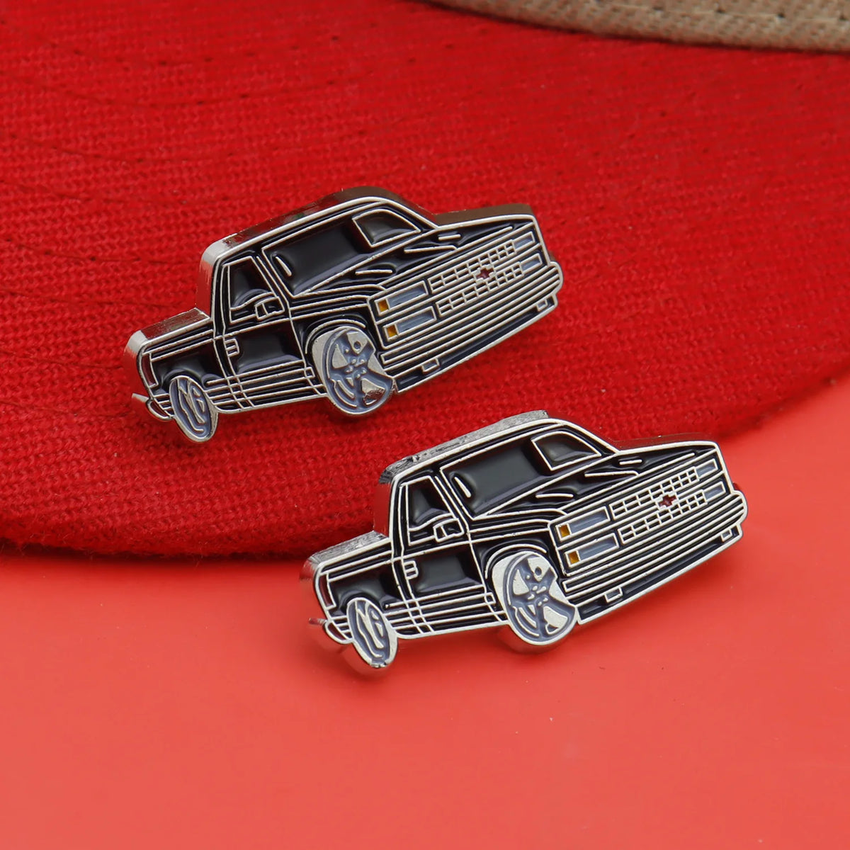 A silver metal clip pin shaped like a vintage black car with chrome details resting on a red fabric background.