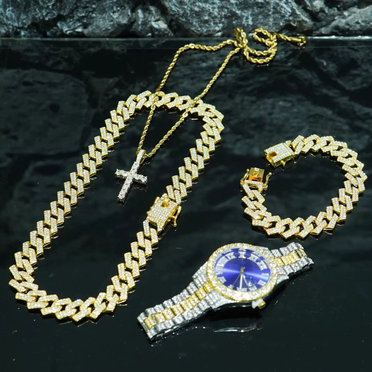 Gold diamond wrist watch and hip hop chain necklace set displayed on a dark surface