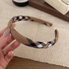 A hand holds a beige and black plaid fabric headband, displaying the tartan pattern.