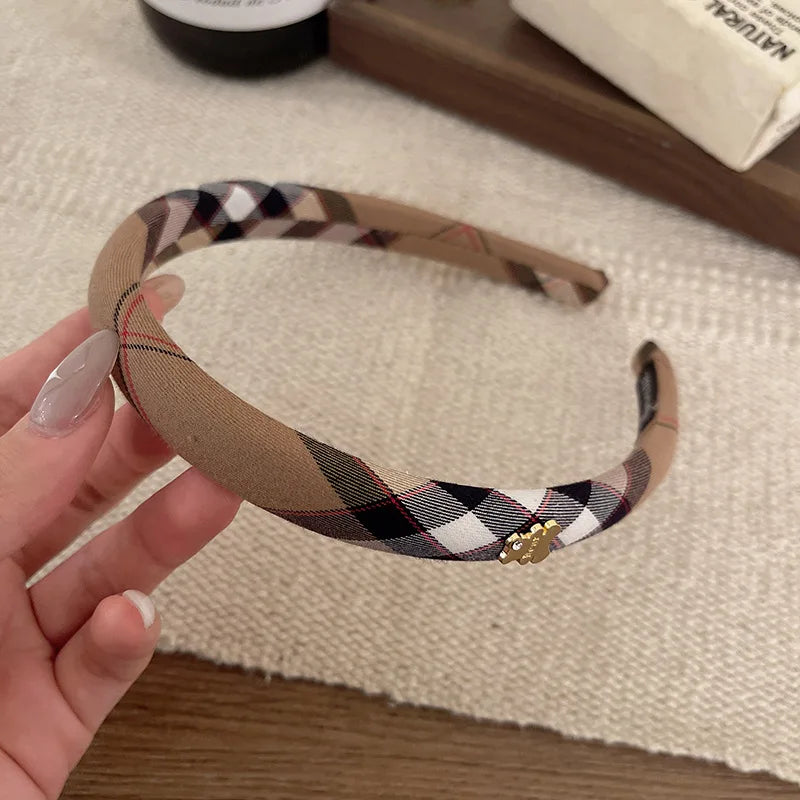 A hand holds a beige and black plaid fabric headband, displaying the tartan pattern.