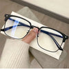 A pair of black anti-blue light clear framed eyeglasses resting on a white paper next to a person's hand.