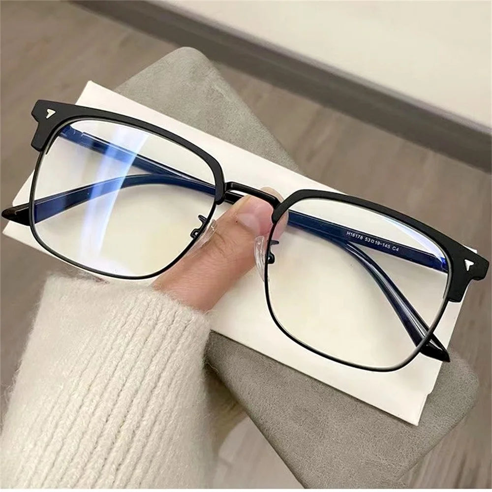 A pair of black anti-blue light clear framed eyeglasses resting on a white paper next to a person's hand.