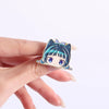 A hand holds a cute anime character brooch lapel pin featuring a blue-haired girl with light purple eyes and blue hair access