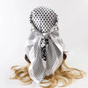 A white satin silk scarf with black polka dots tied in a bow, displayed on blonde hair.