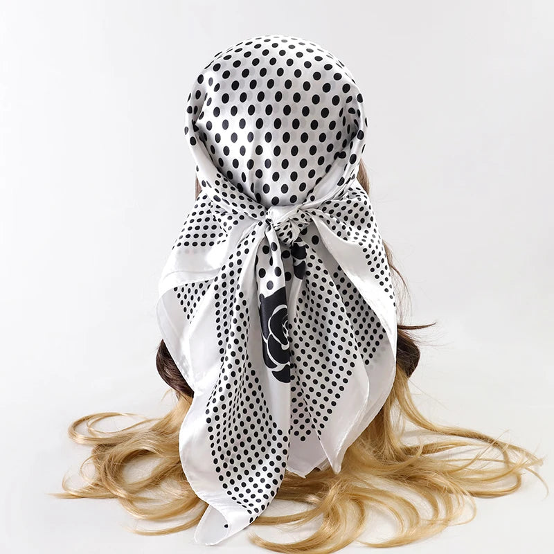 A white satin silk scarf with black polka dots tied in a bow, displayed on blonde hair.