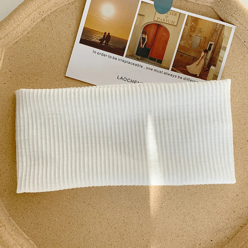White knitted sports headband lying on a light brown surface next to a card.