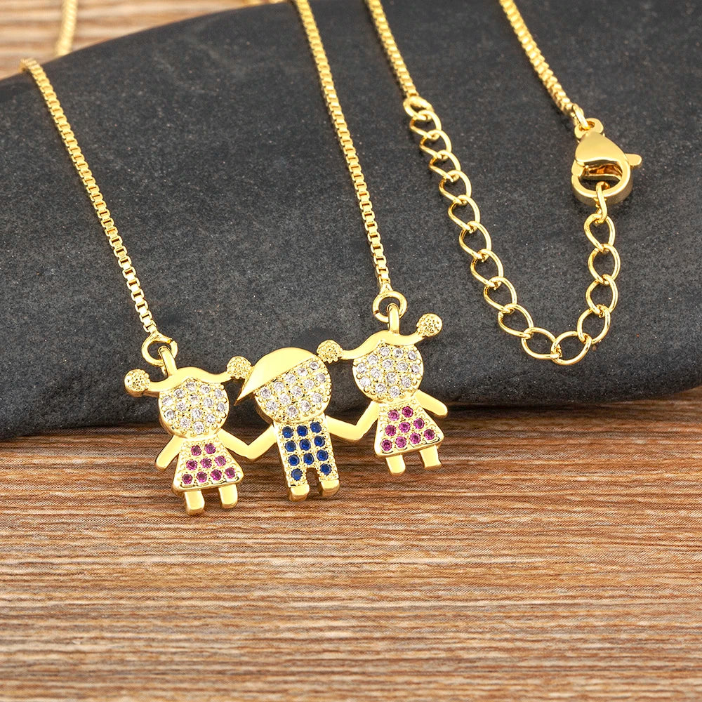 Collier en chaîne en or avec trois petites figurines en pierres CZ, présenté sur une surface sombre.
