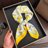 A yellow and white silk scarf tied in a knot is displayed on a dark tray.