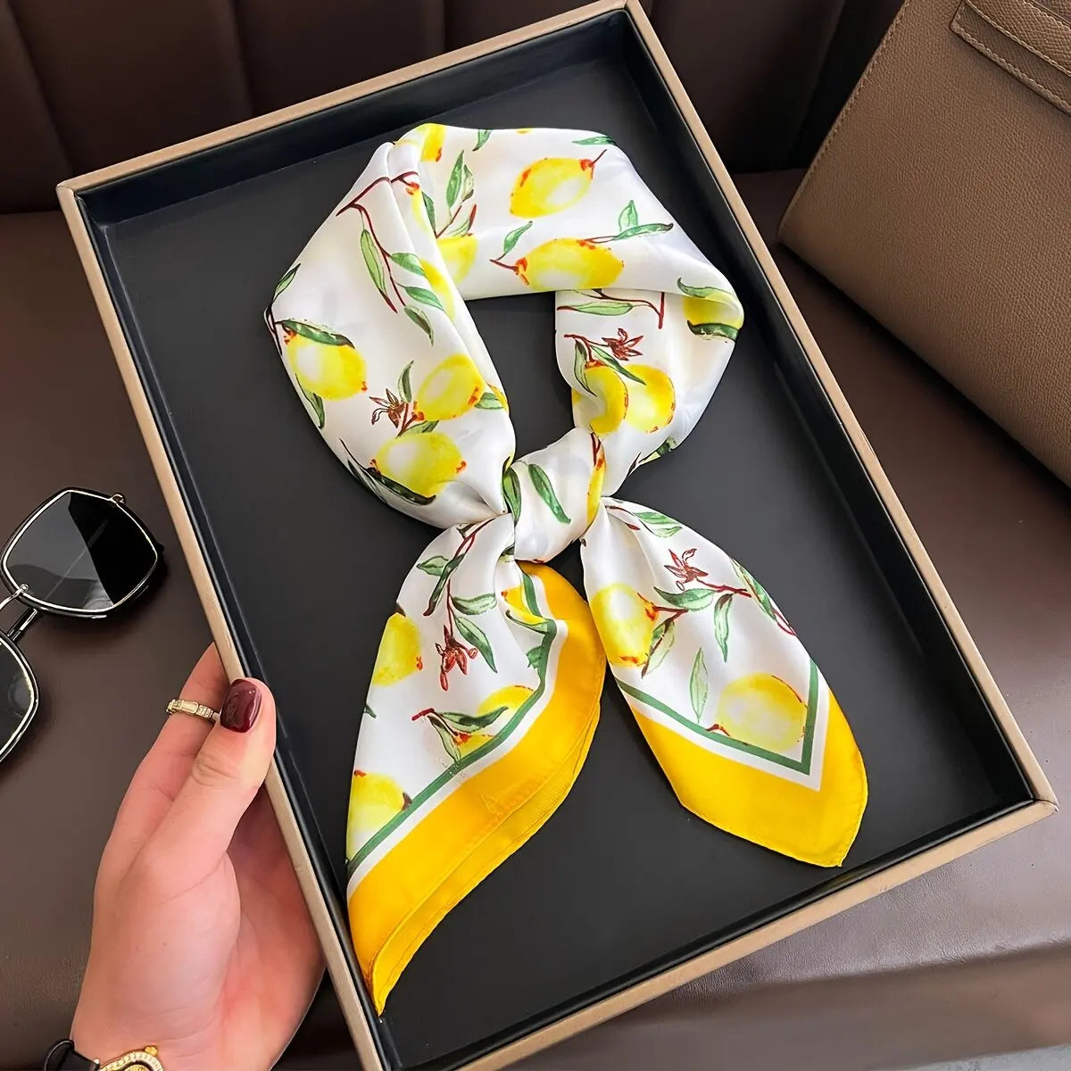 A yellow and white silk scarf tied in a knot is displayed on a dark tray.