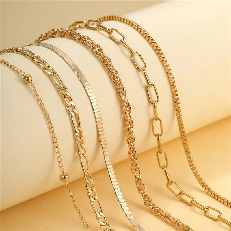 Eine Kollektion zarter goldener geometrischer Knöchelketten, präsentiert auf hellem Hintergrund.