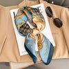 A luxury silk scarf featuring intricate patterns in blue, gold, and brown tied as a square shawl, displayed on a beige blazer