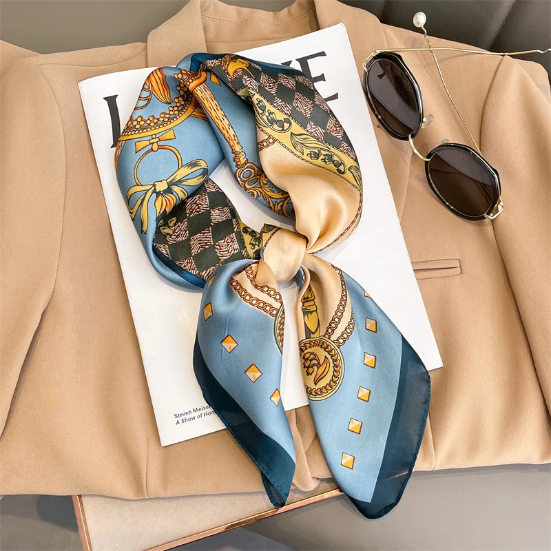 A luxury silk scarf featuring intricate patterns in blue, gold, and brown tied as a square shawl, displayed on a beige blazer