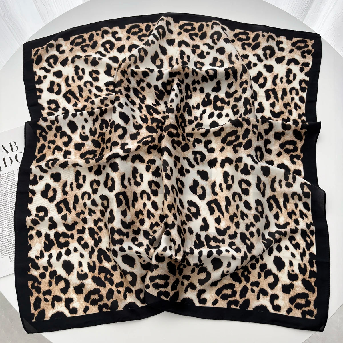 A luxury leopard print silk scarf folded and displayed against a white background.