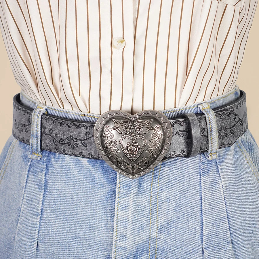 A close-up of a heart-shaped retro embossed belt worn over a striped button-down shirt and light wash denim pants.