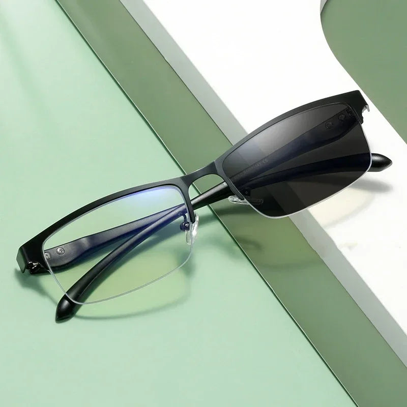 Une paire de lunettes de lecture photochromiques noires posées sur une surface vert clair.