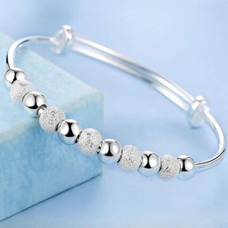 Silver bell bangles for women featuring small round textured beads displayed on a light blue surface