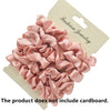 A set of pink satin hair scrunchies displayed on a cardboard backing.