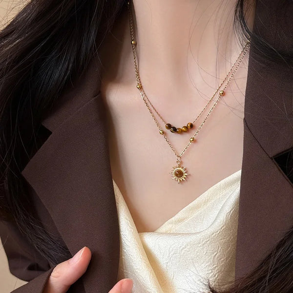 Nahaufnahme eines Gold-Tigerauge-Sonnenblumen-Anhänger-Kettchens, getragen gegen einen dunkelbraunen Blazer und ein cremefarb