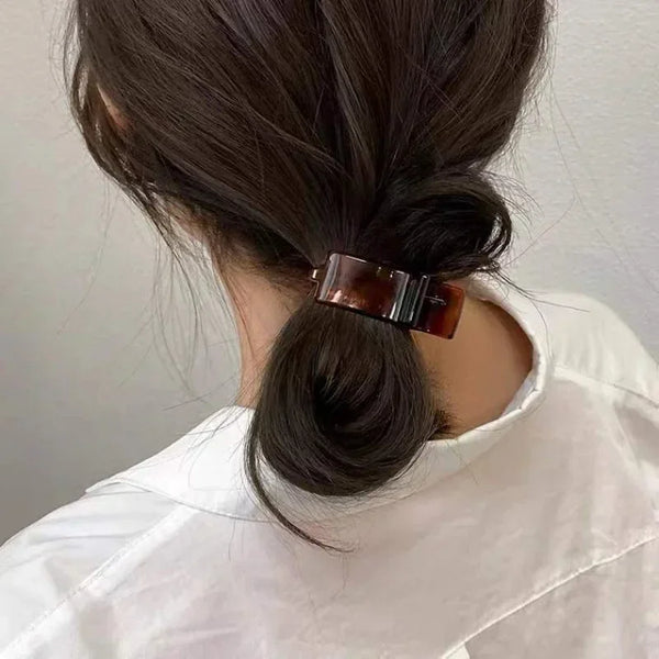 A woman's dark hair is styled in a low ponytail secured with a transparent acrylic hair claw.