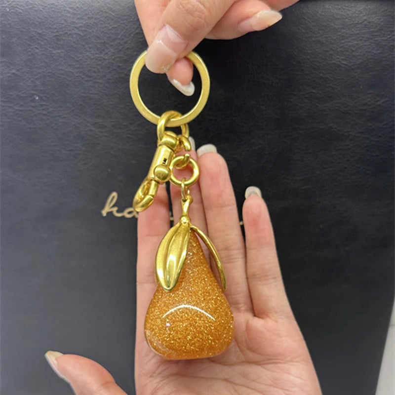 Un charm clé en forme de poire dorée est tenu par une personne sur un fond sombre.