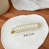 A white rubber braided ponytail holder is displayed on a white ceramic plate with a measurement line indicating 7cm length.
