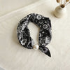 Black silk scarf with white floral print tied in a bow and adorned with a pearl