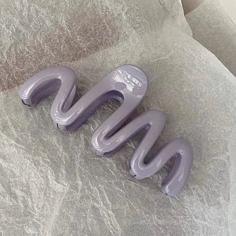 Un set de pinzas para el cabello en forma de ola moradas sobre papel de hisopo arrugado.