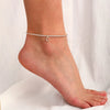 A close-up of a vintage letter anklet bracelet worn on a person's ankle.