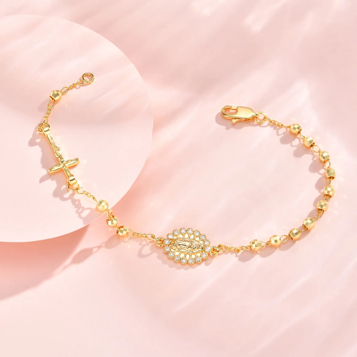 A delicate gold plated rosary bracelet for women displayed on a pink background.