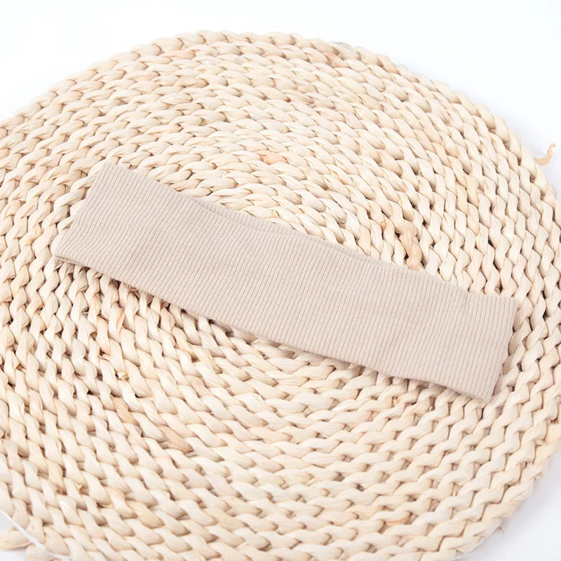 A beige knitted elastic headband lying diagonally across a round woven straw mat.